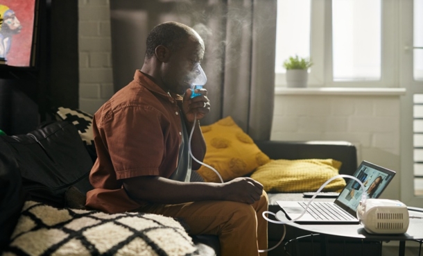 Adult with bronchial asthma using a nebulizer during a telemedicine video visit on a laptop at home