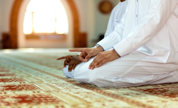 Pilgrim kneeling in prayer during Hajj or Umrah travel, illustrating meningitis vaccination requirements