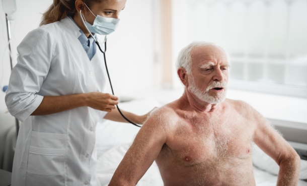 Portrait of doctor in mask listening to an older man’s chest with a stethoscope during a respiratory exam, illustrating idiopathic pulmonary fibrosis care and ACE inhibitor use outcomes.