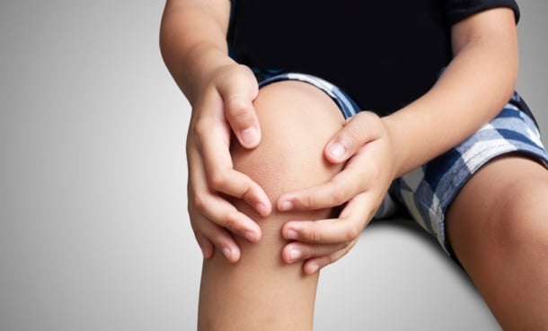 Child holding a painful knee, illustrating juvenile arthritis joint pain and inflammation
