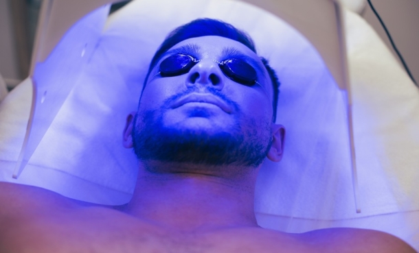 Man lying in an indoor tanning bed under ultraviolet light, wearing protective tanning goggles to reduce eye exposure.