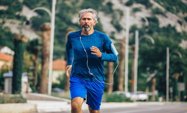 Older man running outdoors with earbuds, representing return to sport after knee arthroplasty