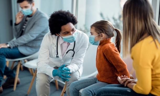 Pediatrician speaking with a young child and parent in a clinic waiting room, representing pediatric hepatitis B monitoring and liver health follow up care.