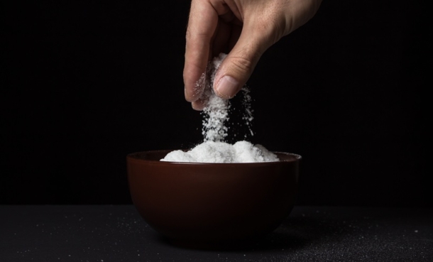 Hand sprinkling salt into a bowl on a dark background, illustrating salt intake advice in cystic fibrosis under review after ETI therapy.