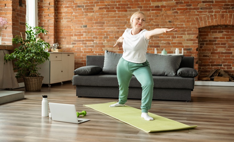 Older adult doing a home-based video-guided exercise programme using a laptop after lumbar spine surgery.