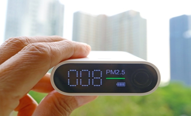 Close-up of a hand holding an air quality sensor displaying PM2.5 levels against a blurred city skyline, illustrating outdoor air pollution exposure linked to glycolipid metabolic disorders.