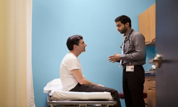 Doctor speaking with a patient seated on an exam table in a clinic room.