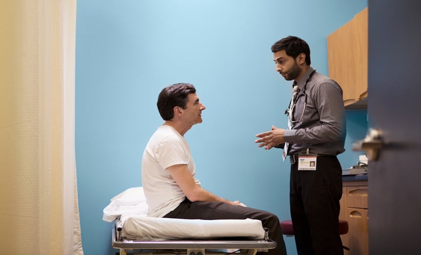 Doctor speaking with a patient seated on an exam table in a clinic room.