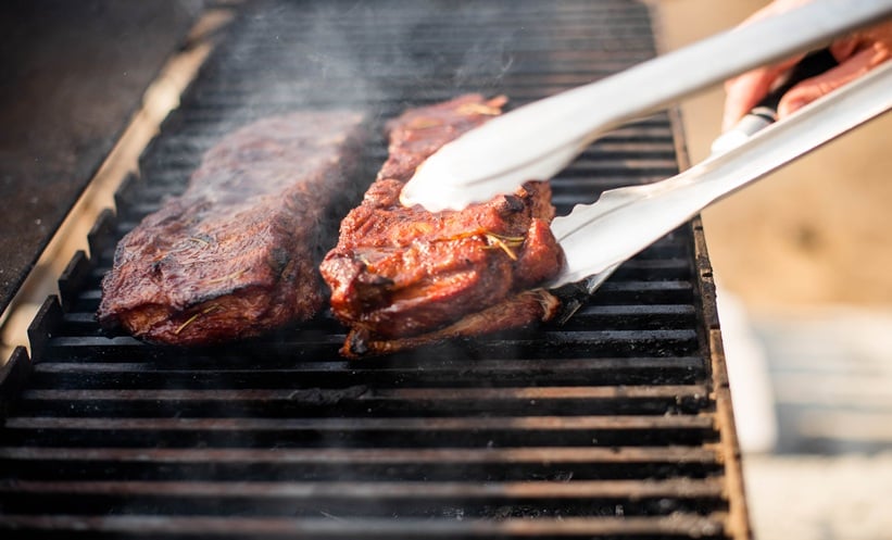 Charcoal grill smoke rising during pork belly cooking, illustrating polycyclic aromatic hydrocarbons exposure risk.