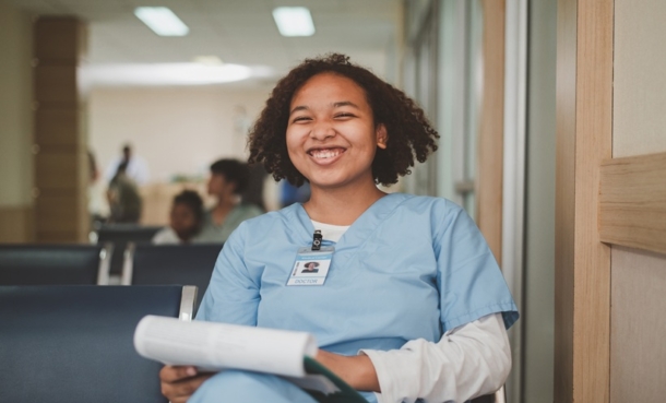 Medical trainee in scrubs smiling in a hospital corridor
