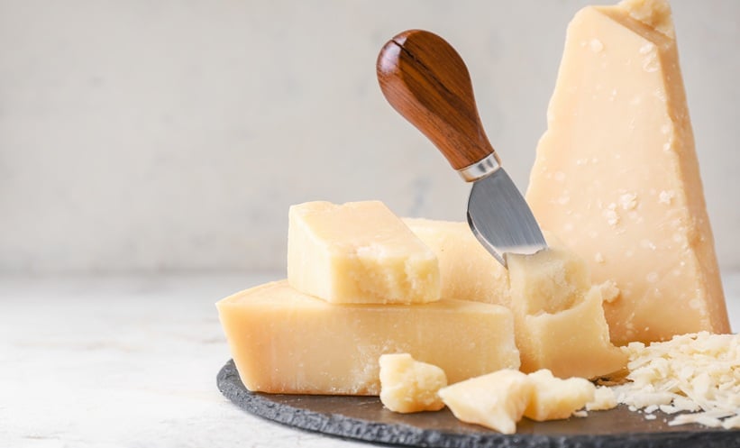 Close up of Parmesan cheese wedges and shavings on a serving board with a cheese knife.