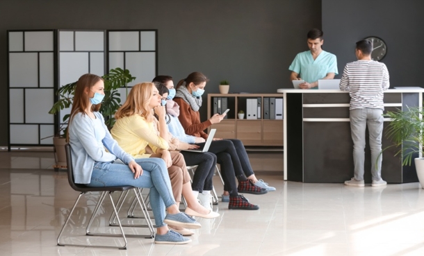 Waiting room at a sexual health clinic, with several adults seated in a row while a patient checks in at reception.