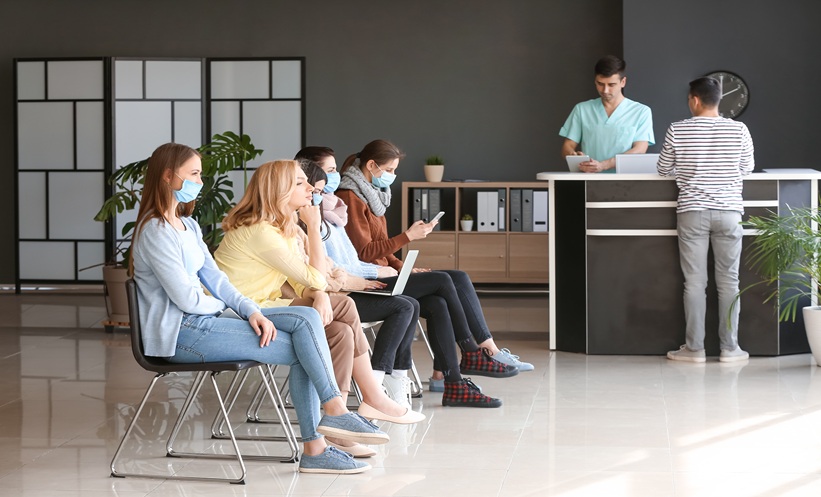 Waiting room at a sexual health clinic, with several adults seated in a row while a patient checks in at reception.