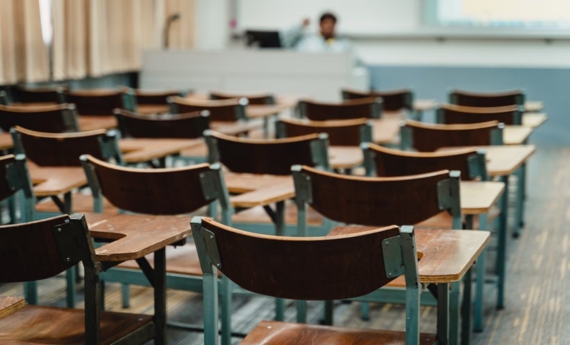 Blurred university classroom with empty desks and chairs, representing a campus setting during a meningitis outbreak.