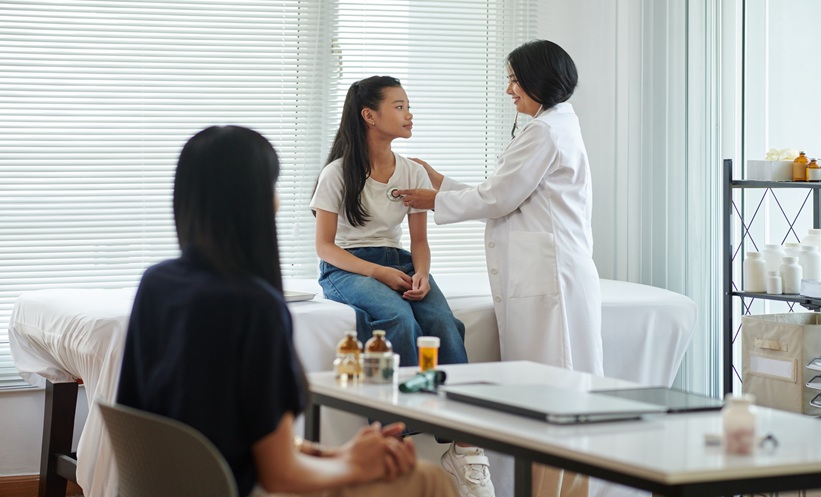 Smiling pediatrician examining teenage girl sitting on bed