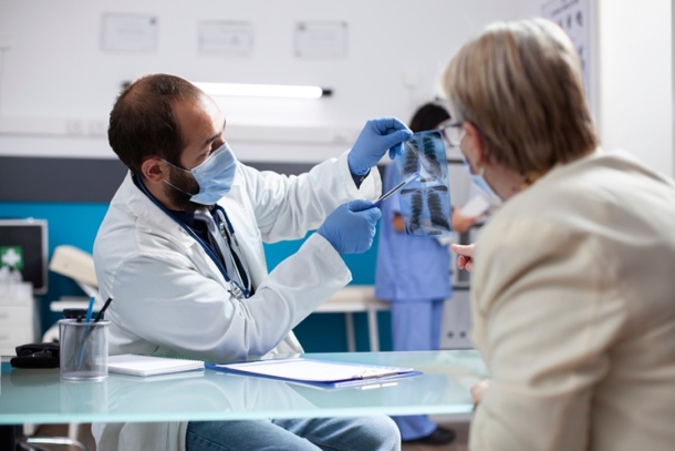 doctor holding up lung x-rays, while pointing at them with a pen and explaining them to a patient