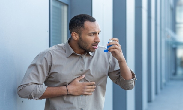 distressed man holding at his chest with his right hand while holding up an asthma inhaler with his left hand