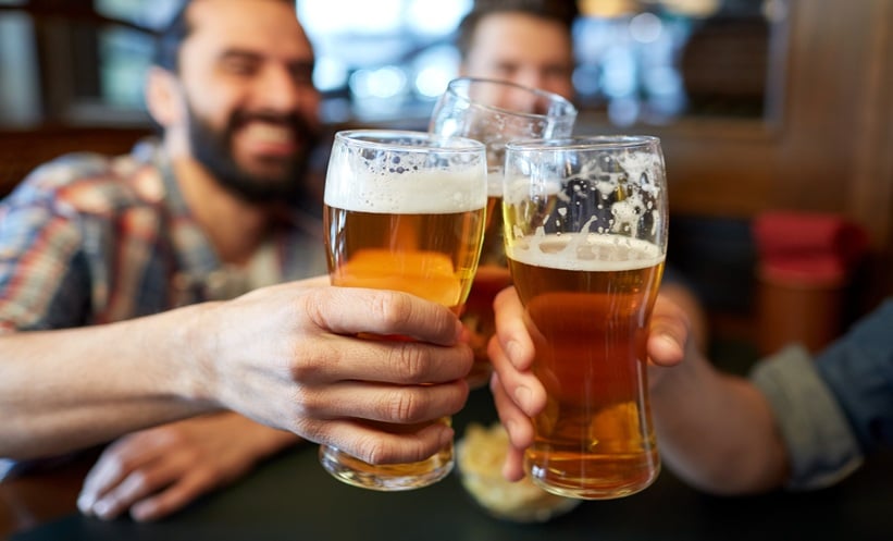 Friends drinking beer and clinking glasses at a bar.