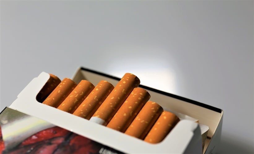 Esophageal cancer risk factors concept with cigarette smoke and alcohol glass in a low light setting.