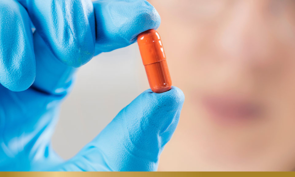 Blue-gloved hand holding an orange capsule