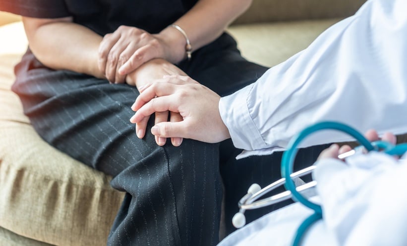 Doctor comforting a patient by placing his hand over the patient's hand.