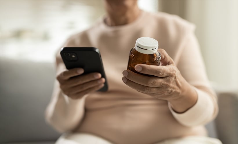 Patient using a smartphone while holding a medication bottle, representing mobile health apps for lupus erythematosus disease management.