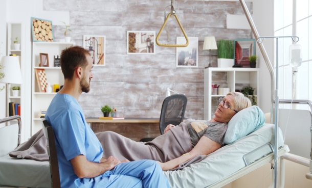 Healthcare professional speaking with older patient in bed during assessment for ALS sleep disturbances and respiratory dysfunction.