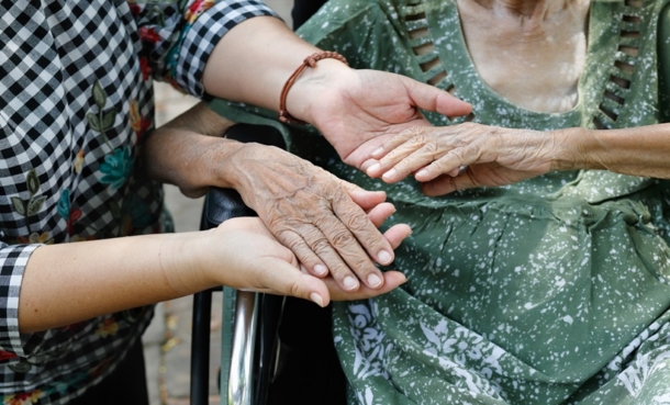 Older adult receiving hand support from a caregiver, representing stroke recovery and small vessel disease care.