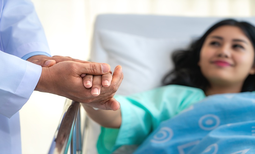 Clinician holding a patient’s hand during a cancer pain management discussion about opioid stigma and shared decision-making.