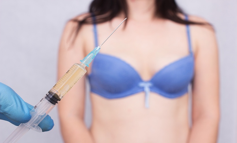 Doctor holds a syringe and in the background is a woman in a bra