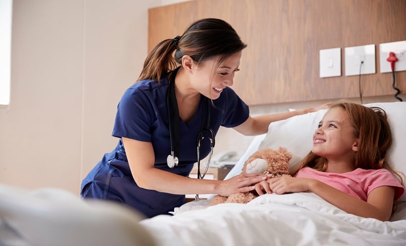 Pediatric clinician speaking with a child during hospital recovery after surgery.