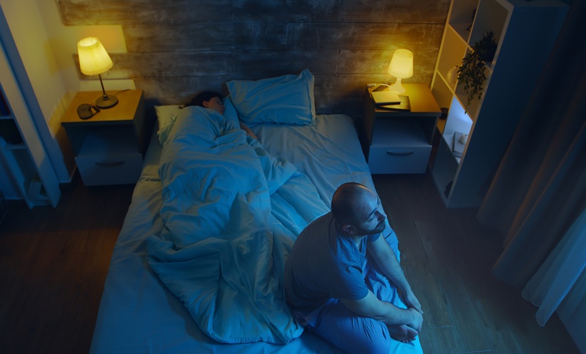 man suffering from insomnia while his wife is sleeping.