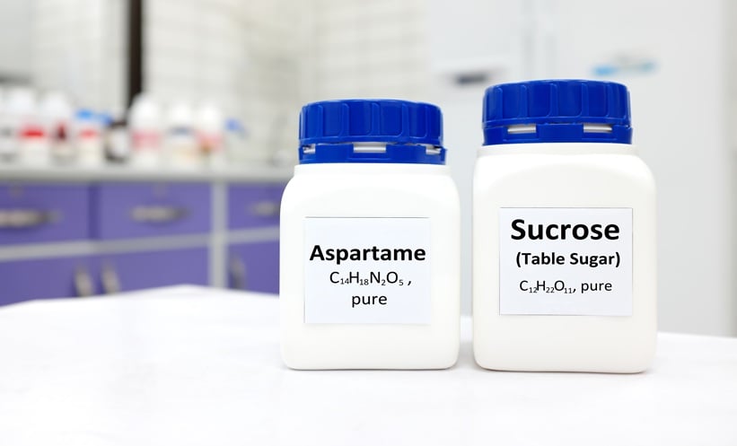 bottle of pure aspartame artificial sweetener and sucrose or table sugar chemical compound comparison. White laboratory background