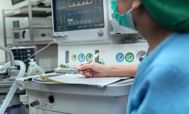 Healthcare professional writing notes beside an monitoring machine.