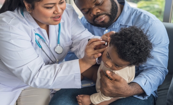 Doctor checks ears of a baby while father is holding him