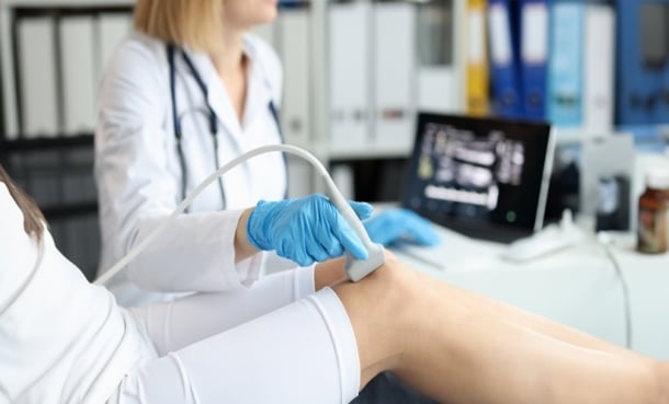 Doctor doing ultrasound examination of patient knee joint in clinic closeup.