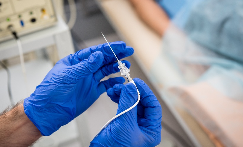 Hands wearing blue latex gloves hold a needle in a cath lab.