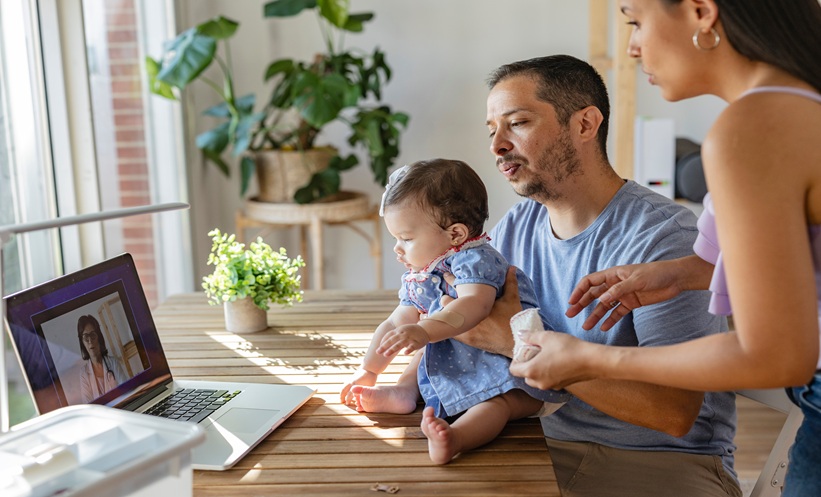 Caregiver using a tablet beside a toddler during a remote pediatric atopic dermatitis assessment.