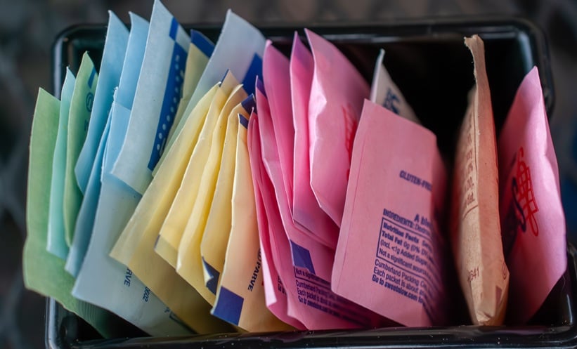 Assortment of vibrant artificial sweetener packets in a caddy, offering various sugar substitutes like Splenda, Sweet'n Low, and Stevia for coffee and tea