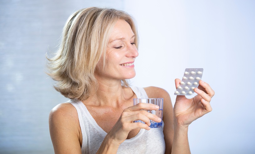 Woman holding HRT pills about to take them witha glass of water