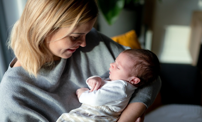 Mother holds newborn baby and stares at it lovingly