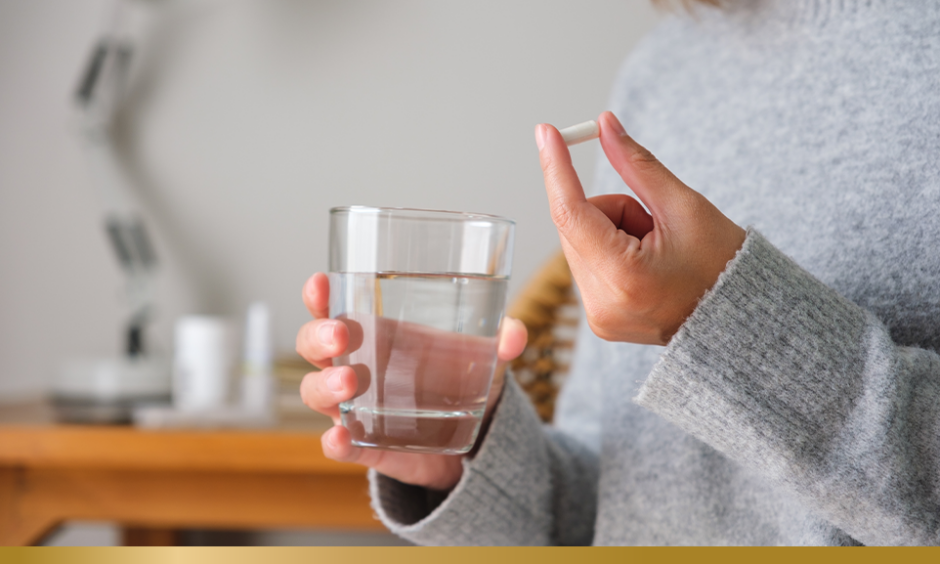 Woman's hand holding pill and a glass of water