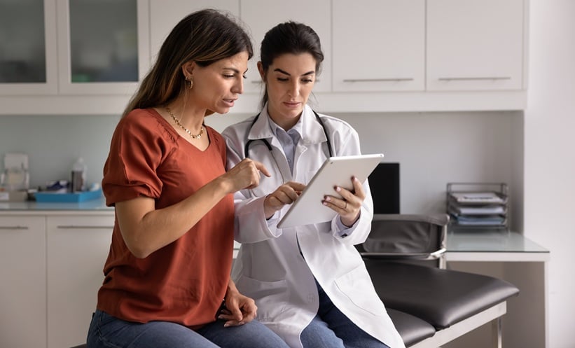 Woman wearing red top looking at test results with doctor wearing whiye coat