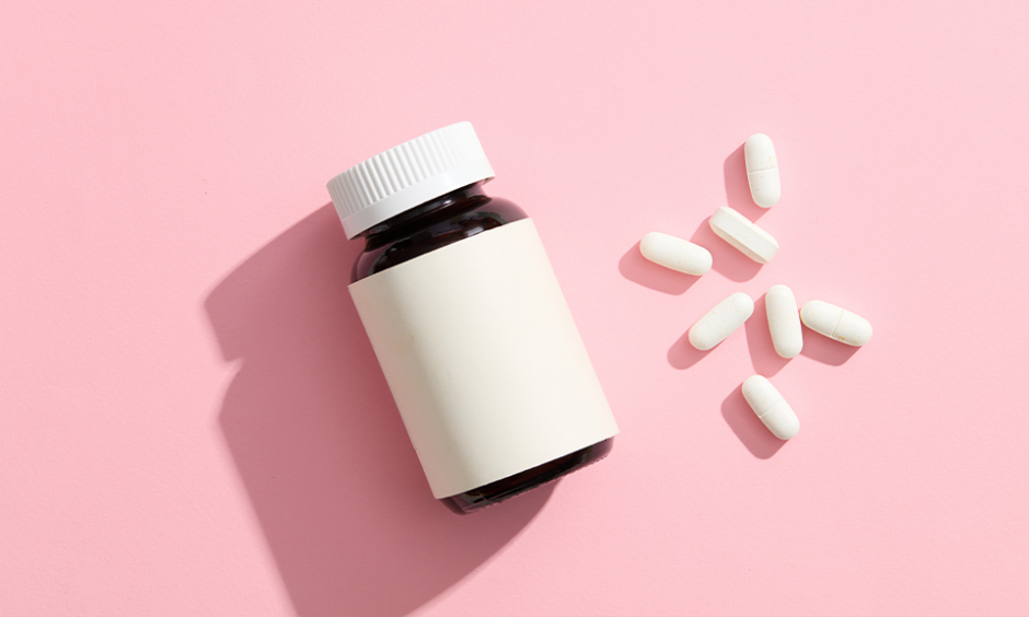 An unlabeled medicine bottle, accompanied by several white pills on a pink background