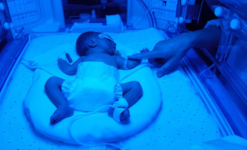 Mother touching her newborn receiving care in a neonatal incubator.