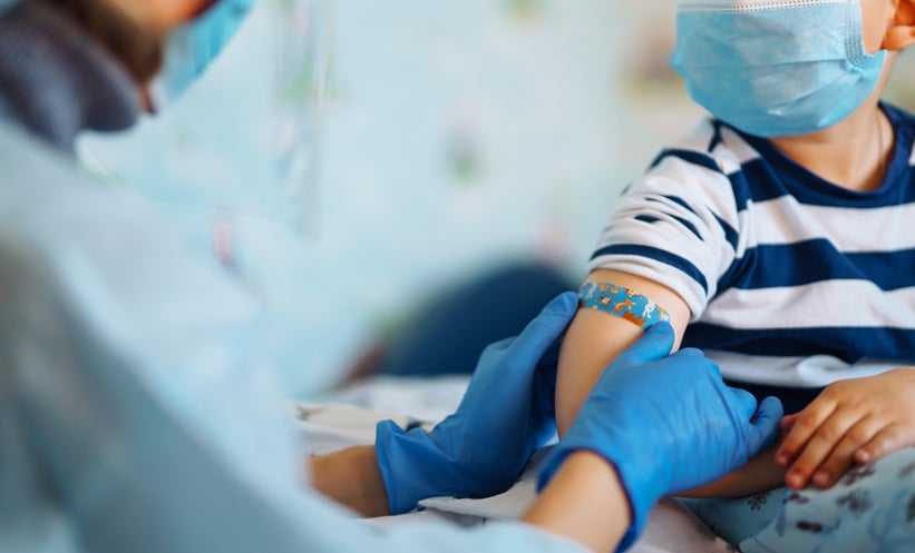 Healthcare professional administering a vaccine to a child wearing a face mask.