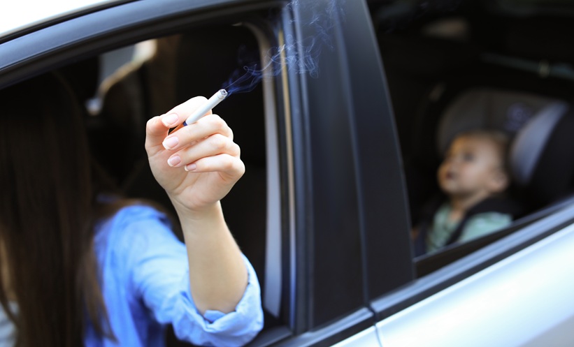 Adult smoking inside a car with a young child seated in the back, illustrating second-hand smoke exposure.