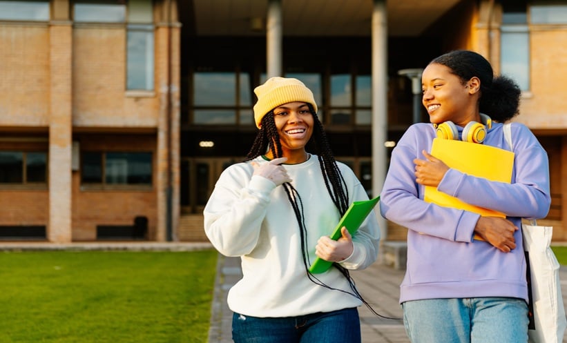 Two young Black women, one with visible vitiligo on her face and hands, talking outdoors.