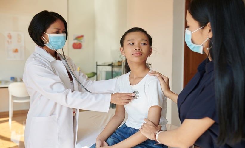 Clinician examining an adolescent during a follow-up appointment with her parent present.