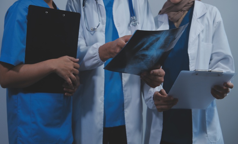 Three clinicians review a chest image while discussing a patient’s respiratory care.